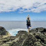 Frau in Yogapose auf Klippe vor Meer auf La Réunion