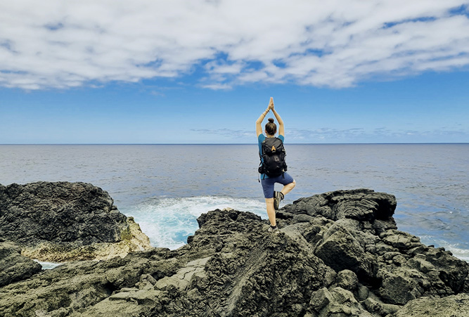 Frau in Yogapose auf Klippe vor Meer auf La Réunion