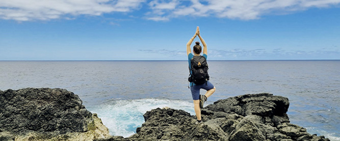 Frau auf Klippe vor Meer in Yogapose auf La Réunion